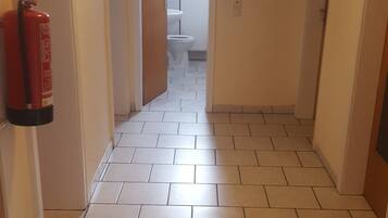 Un pasillo con suelo de baldosas, un extintor a la izquierda y un cuadro en la pared.