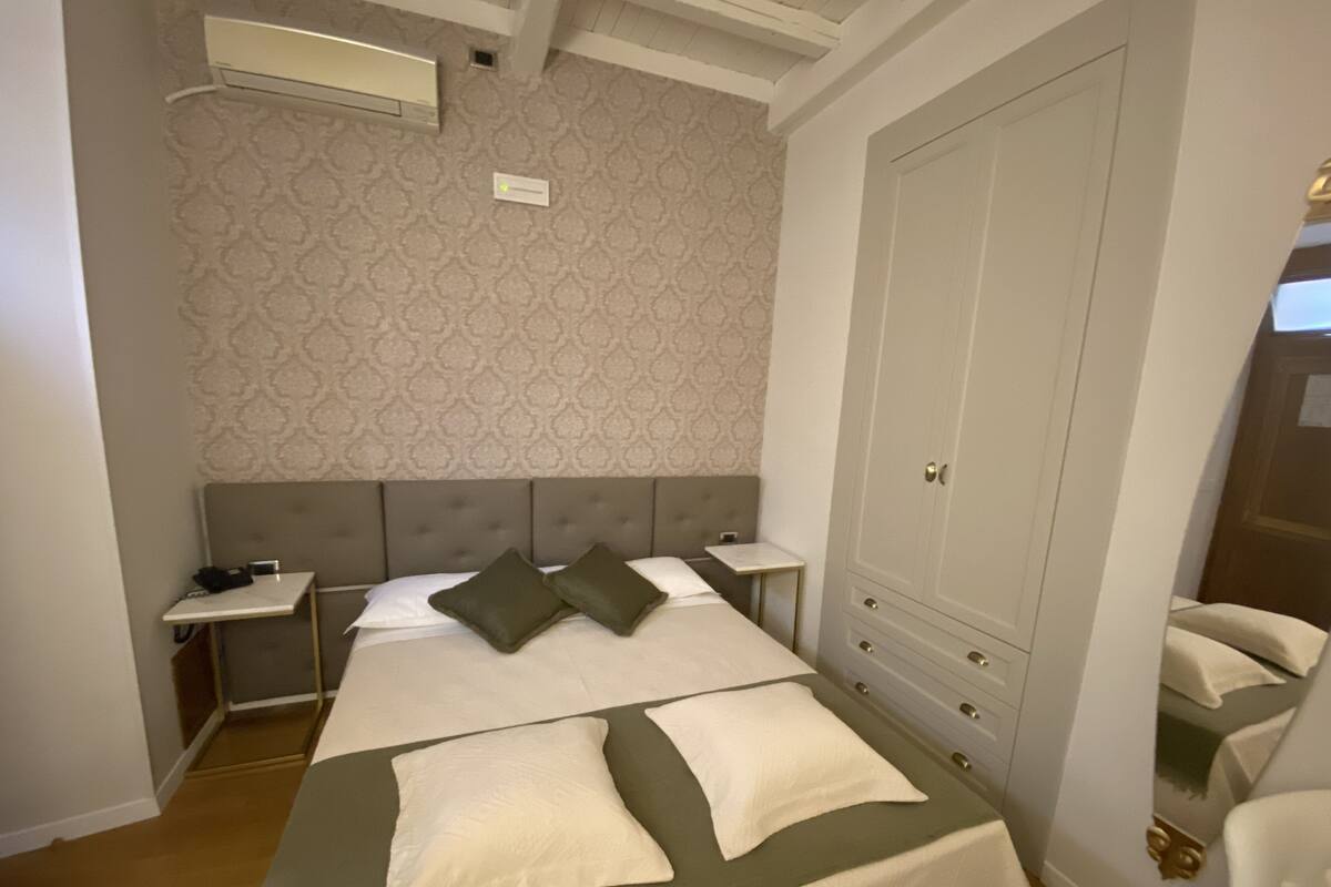 A bedroom with a large bed, two bedside tables, a wardrobe, and a patterned wallpaper.
