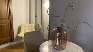 Une pièce avec une table en marbre, un vase contenant des plantes vertes, un fauteuil beige et une porte en bois.