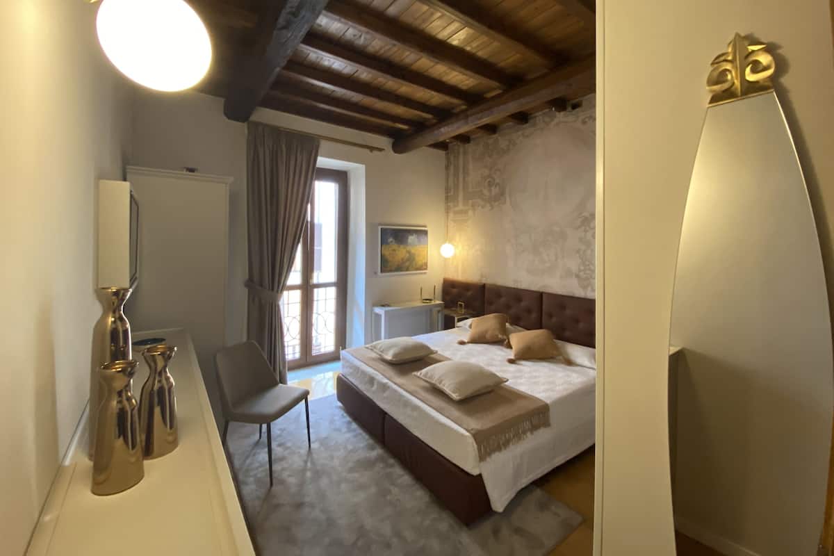 A bedroom with a large bed, a chair, a desk, and a mirror.