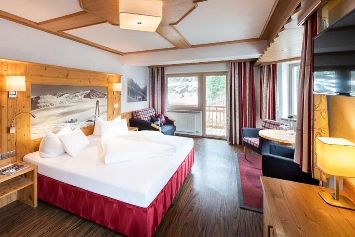 Une chambre d’hôtel avec un grand lit, une tête de lit en bois, un tableau, une petite table, une chaise et une vue sur l’extérieur.