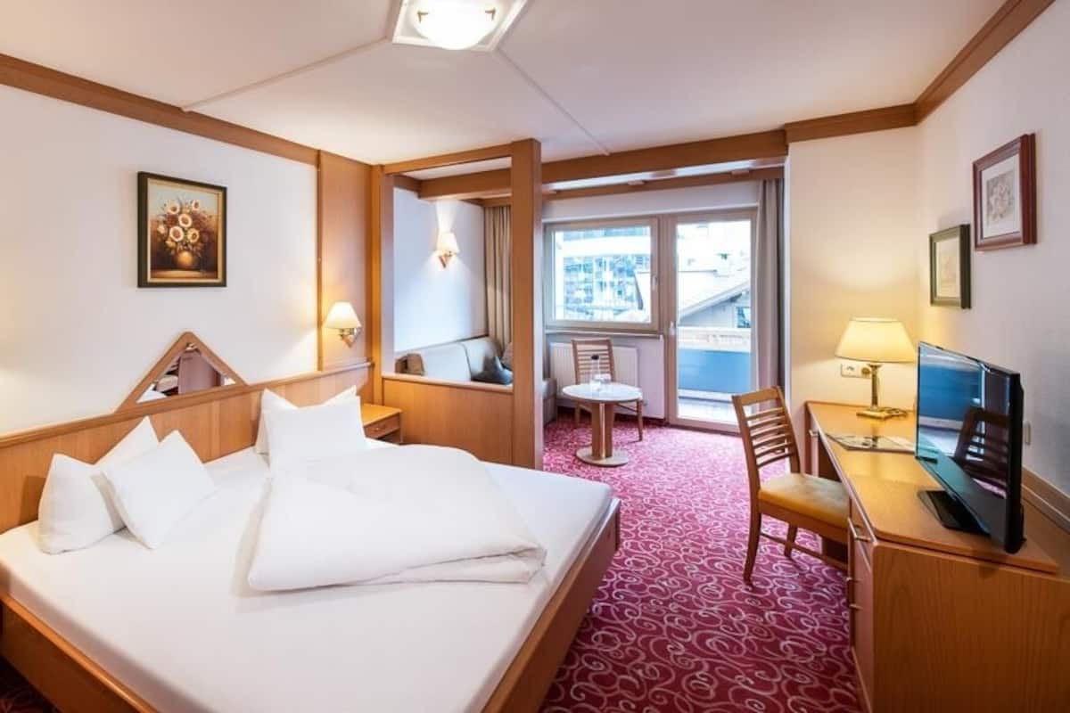 Une chambre d’hôtel équipée d’un lit, d’une table de chevet, d’une télévision, d’un bureau et d’une chaise. Une fenêtre offre une vue sur les bâtiments environnants.