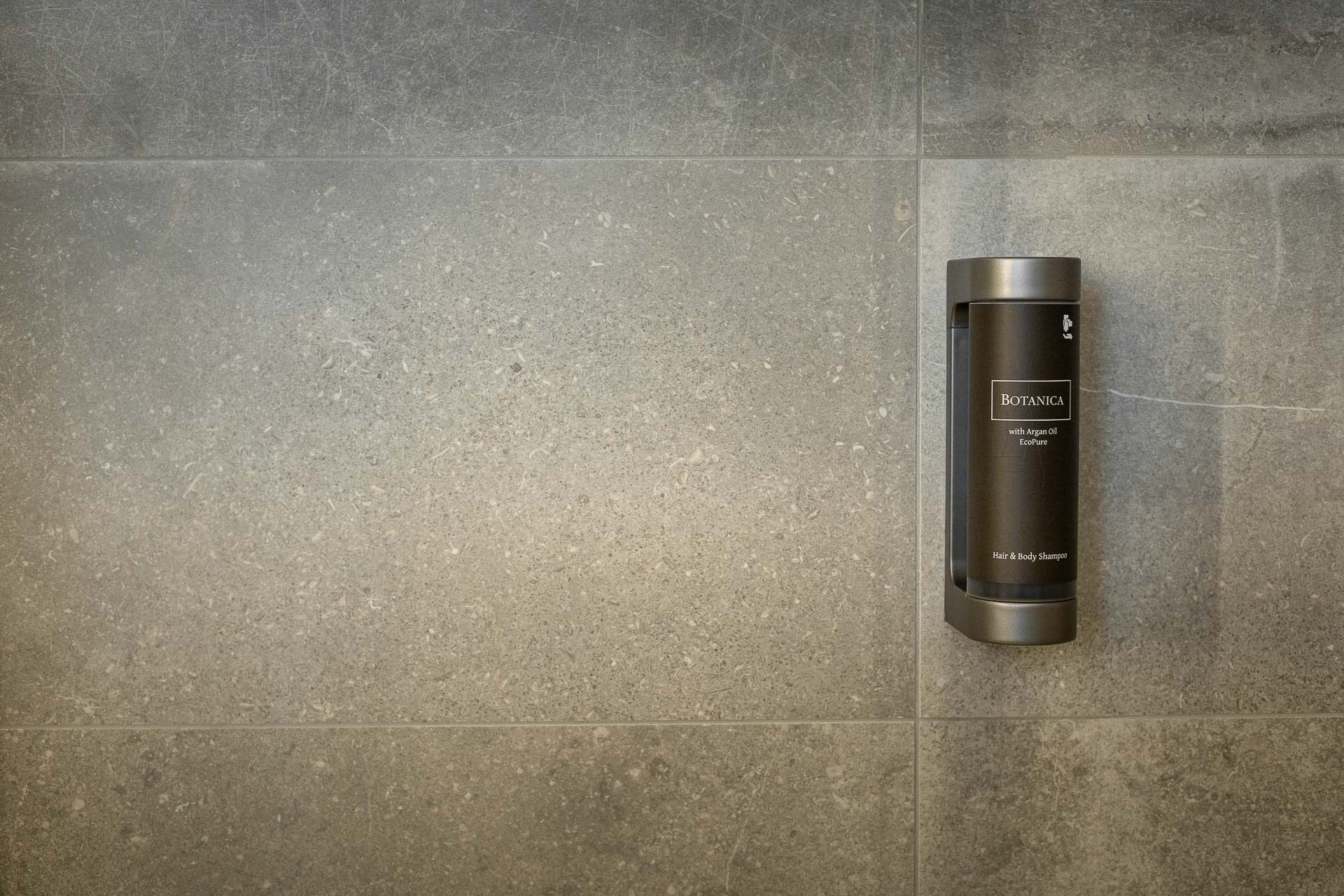 A bathroom with a large, rectangular mirror and a wall-mounted bottle of Botanica hair and body shampoo.