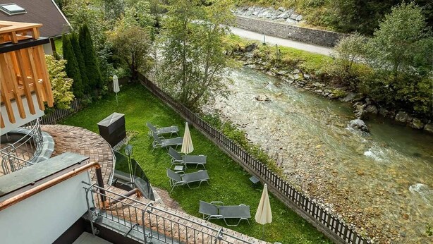 Une terrasse offrant une vue sur une rivière, entourée de verdure et bordée d’une zone boisée.