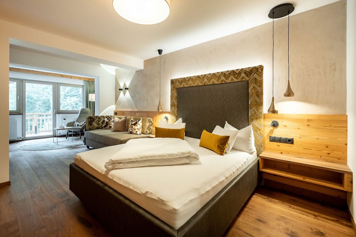 Une chambre d’hôtel moderne dotée d’un grand lit, d’une tête de lit en bois, d’une table de chevet et d’un coin salon avec une chaise et une table.