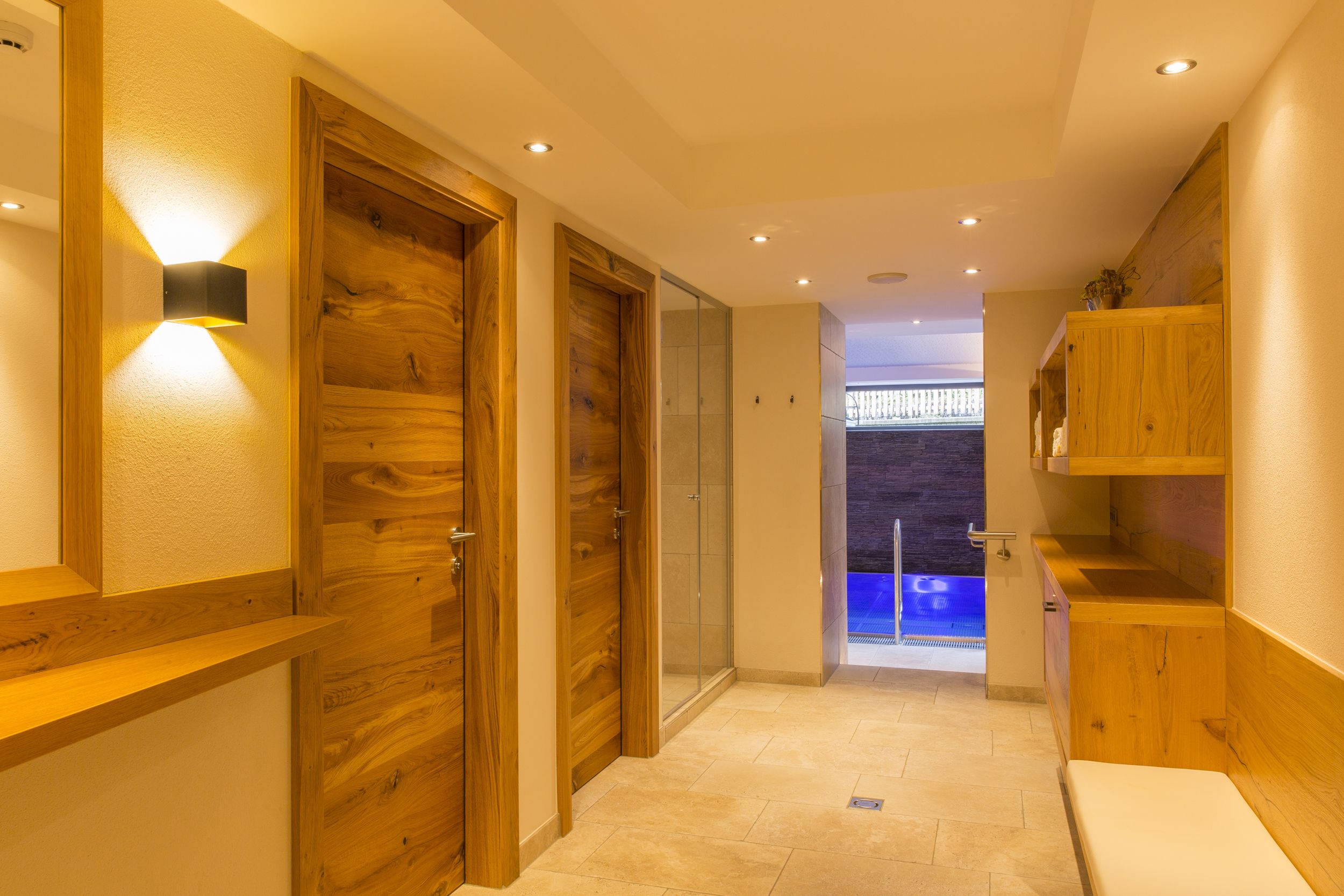 Un pasillo con puertas de madera, una puerta de cristal que da a un balcón, y un banco.