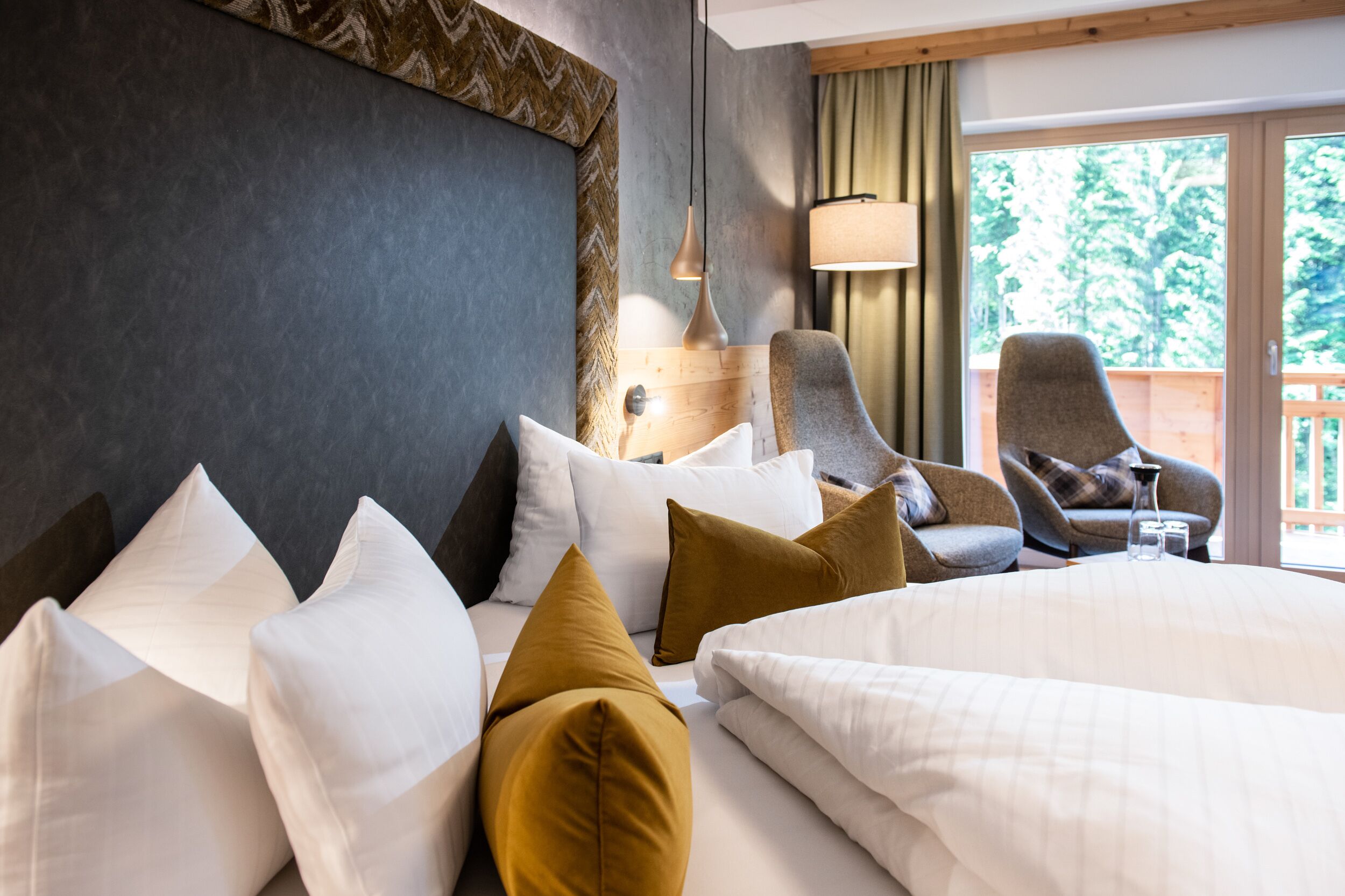 Ett hotellrum med en stor säng, flera kuddar, ett nattduksbord, en lampa och utsikt över omgivningarna.