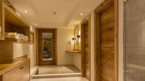 Un couloir avec des étagères en bois, un banc et une porte donnant sur une salle de bain.