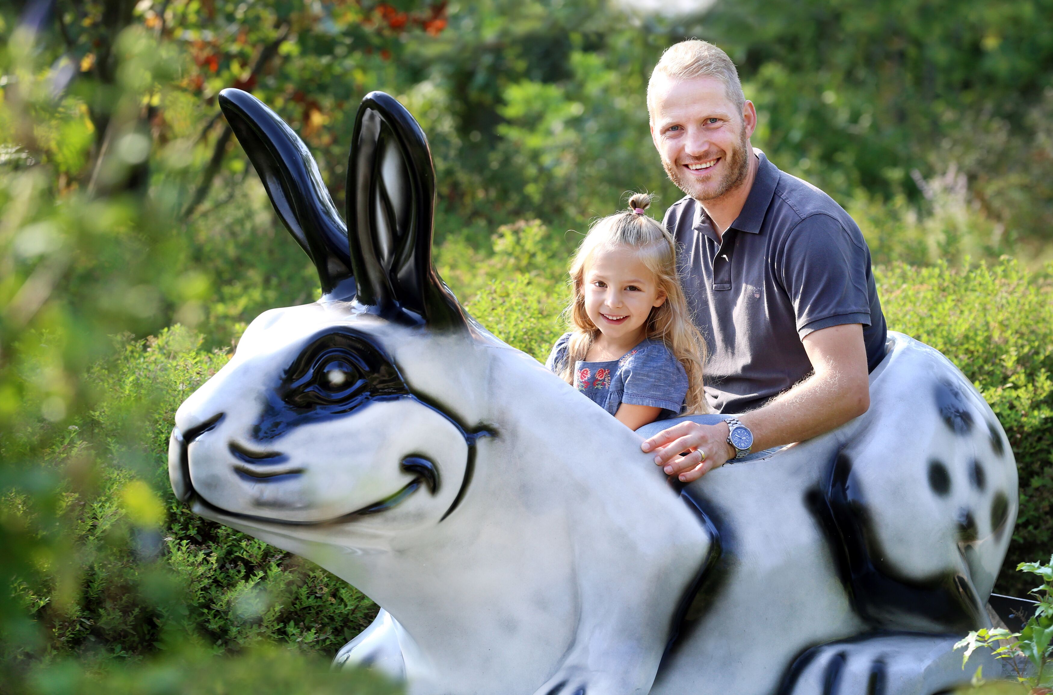 A person sitting on a rabbit statue in a garden.