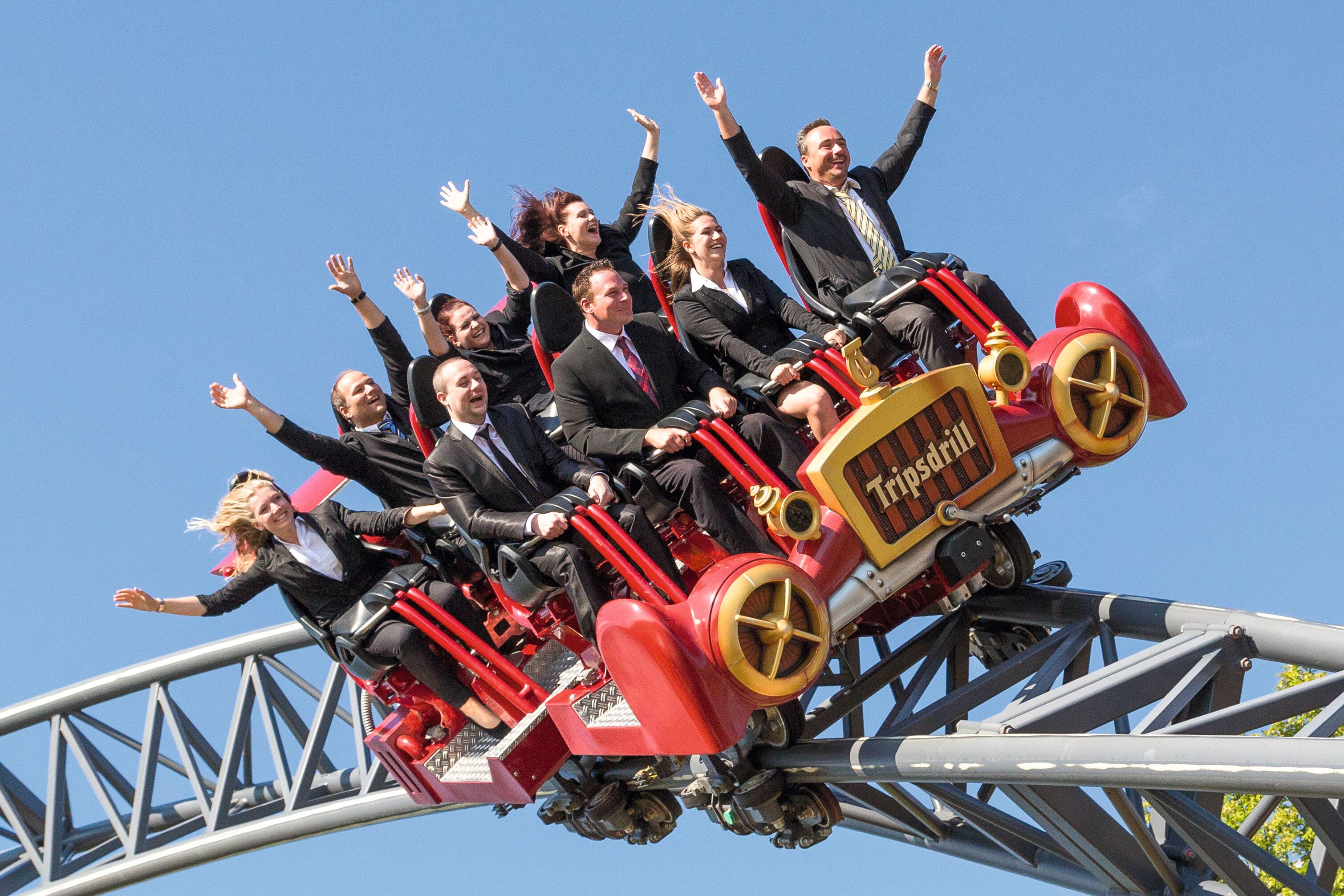 A group of people on a red and yellow roller coaster with the name "Tiptan" visible on the side.