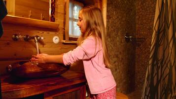 Interno di una baita in legno con un bagno rustico, che include un lavabo in legno e un angolo doccia in pietra.
