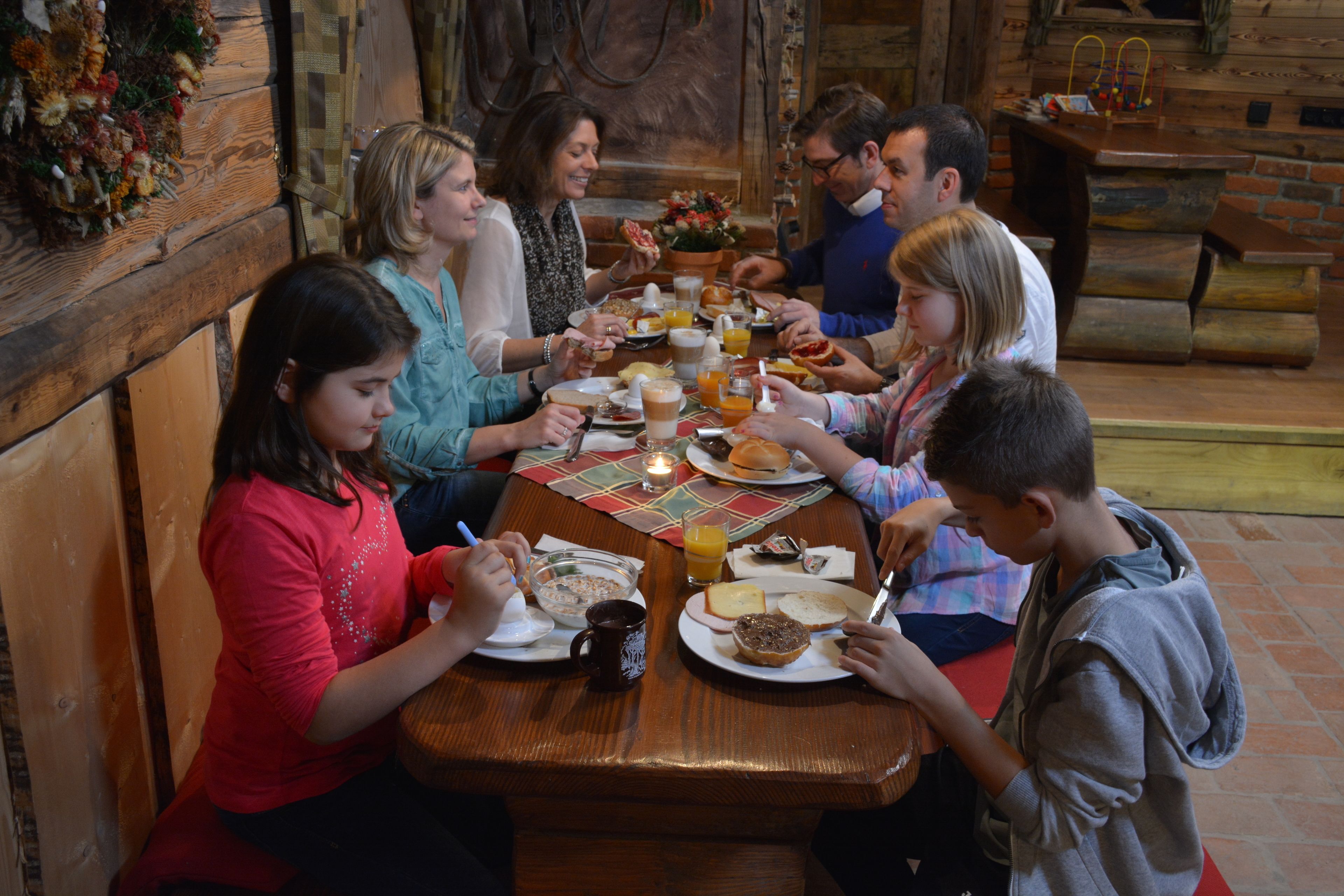 Un grupo de personas cenando en una mesa de madera en un entorno rústico con una pared de ladrillo y bancos de madera.