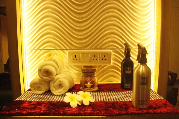 A bathroom with a towel rack holding rolled towels, a candle, and two bottles of Midsky 500ml water. - Meritas Picaddle Resort - Lonavala (Mawal)