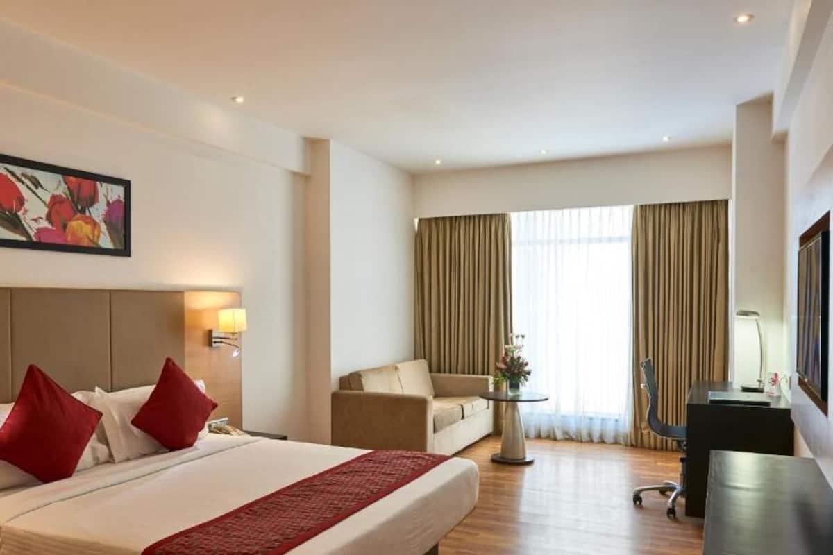 A hotel room with a large bed, a desk, a chair, a sofa, and a window with curtains.