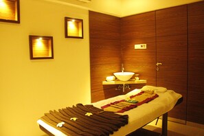 A spa room with a massage table, wooden panel walls, a sink, and framed lights. - Meritas Picaddle Resort - Lonavala (Mawal)