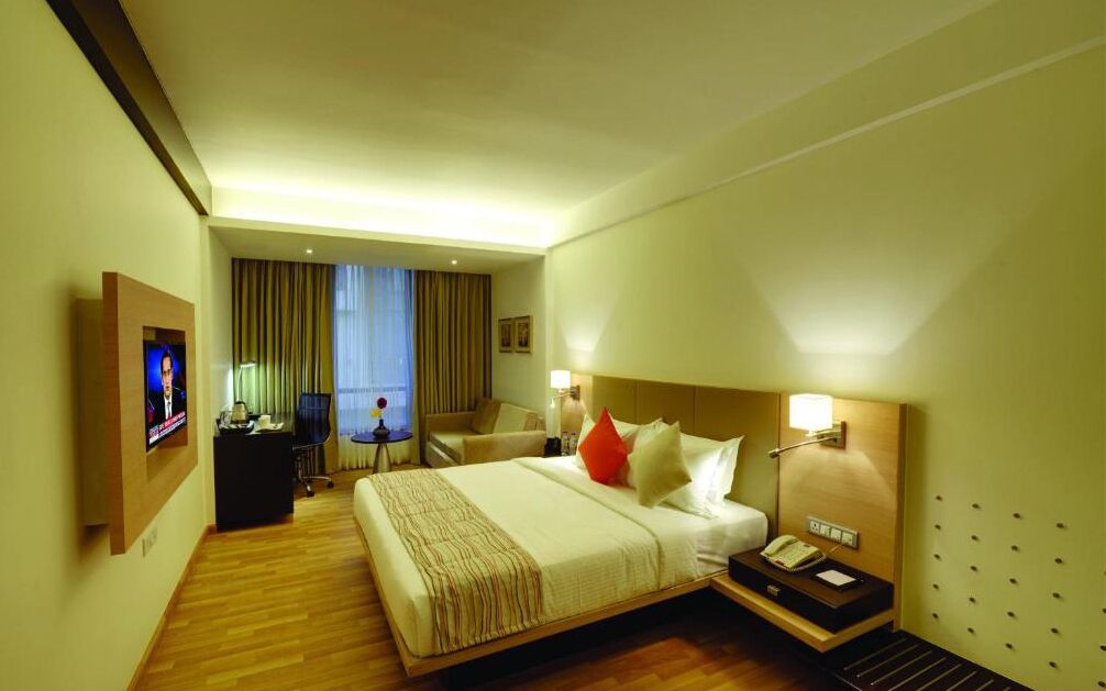 A hotel room with a large bed, a desk, a chair, a TV, and a window with curtains.