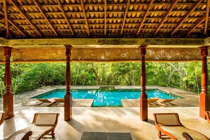 A pool area with wooden loungers and a tiled floor, surrounded by lush greenery. - The River House by Asia Leisure (Balapitiya)