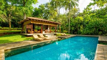 A pool with lounge chairs and a wooden gazebo.