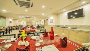 A hotel dining area with multiple tables set for guests, equipped with basic tableware and a central flower arrangement.