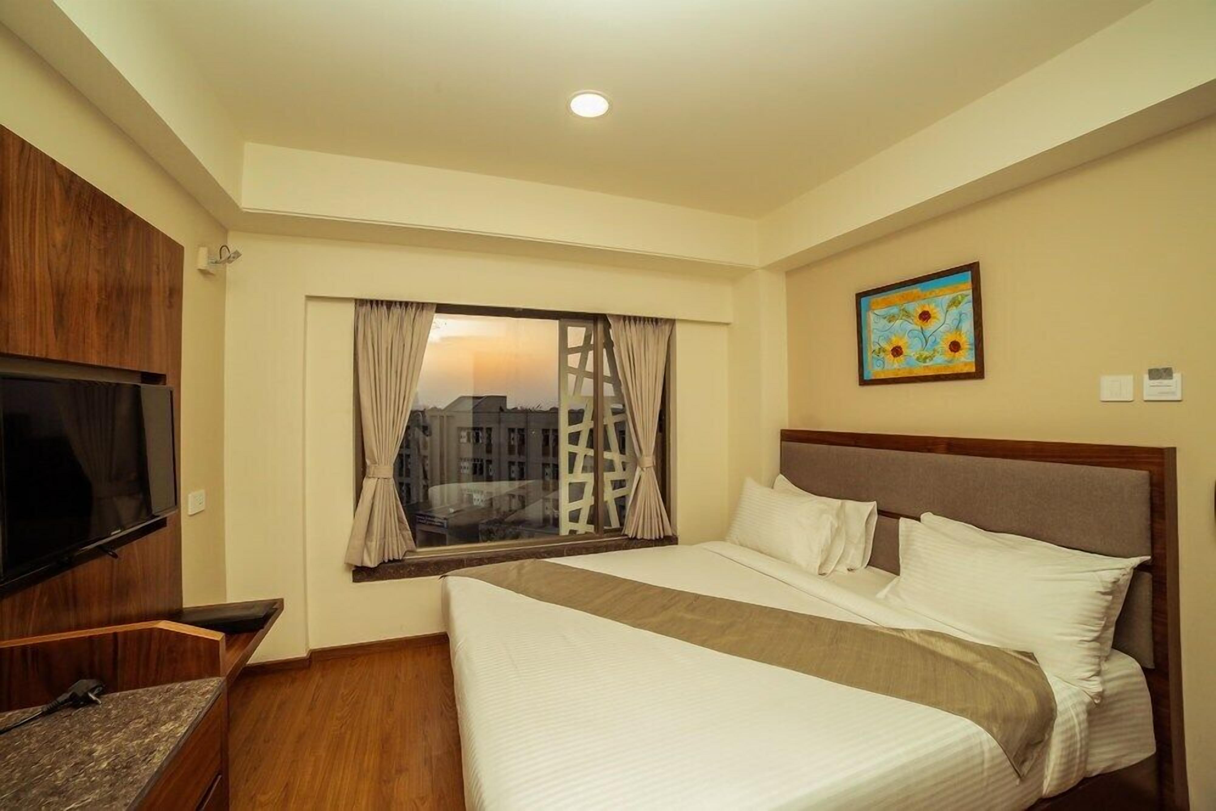 A hotel room with a large bed, a television, a window with curtains, and a painting on the wall.