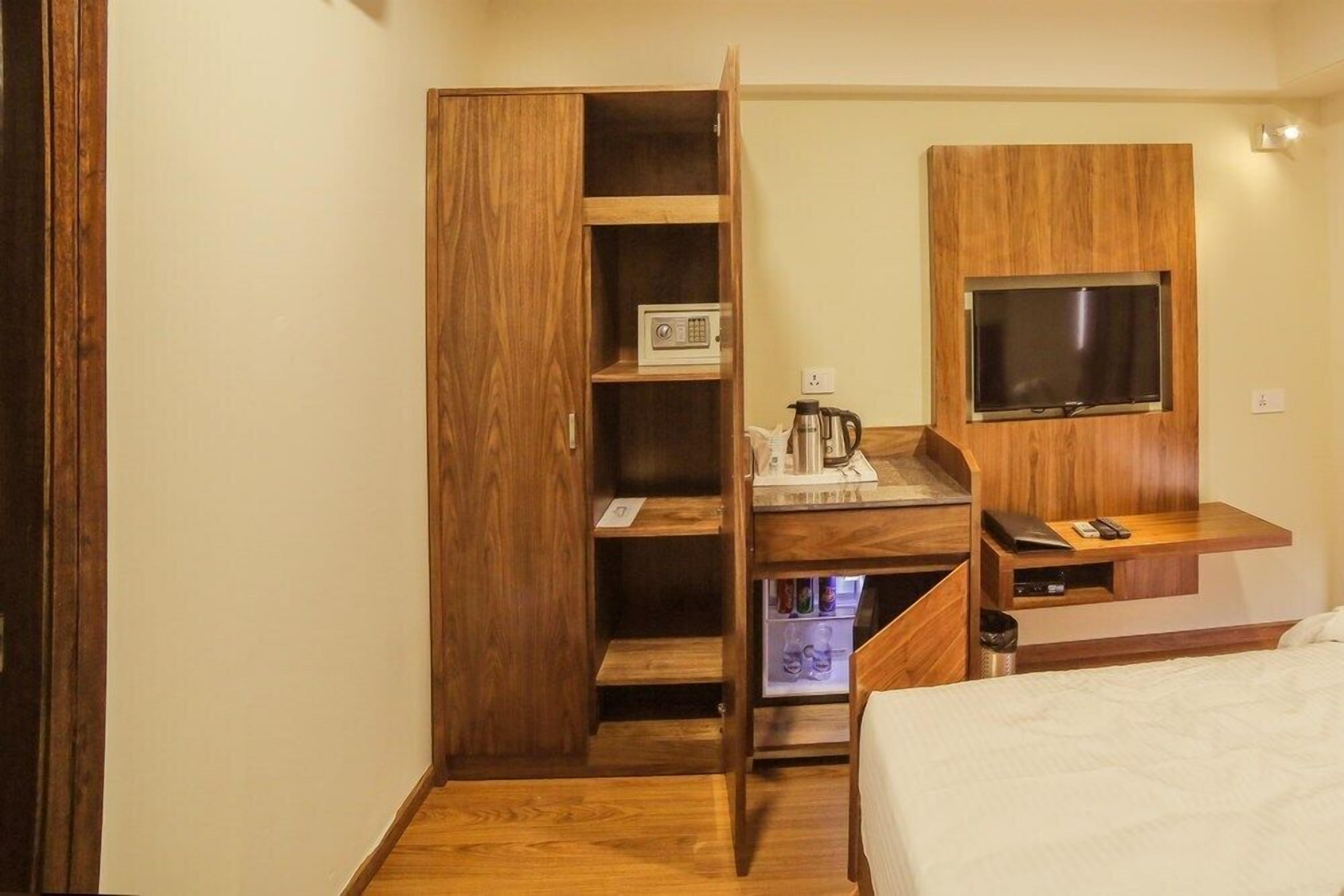 Ein Hotelzimmer mit Holzschrank, Schreibtisch mit Kaffeemaschine, Flachbildfernseher und Bett.