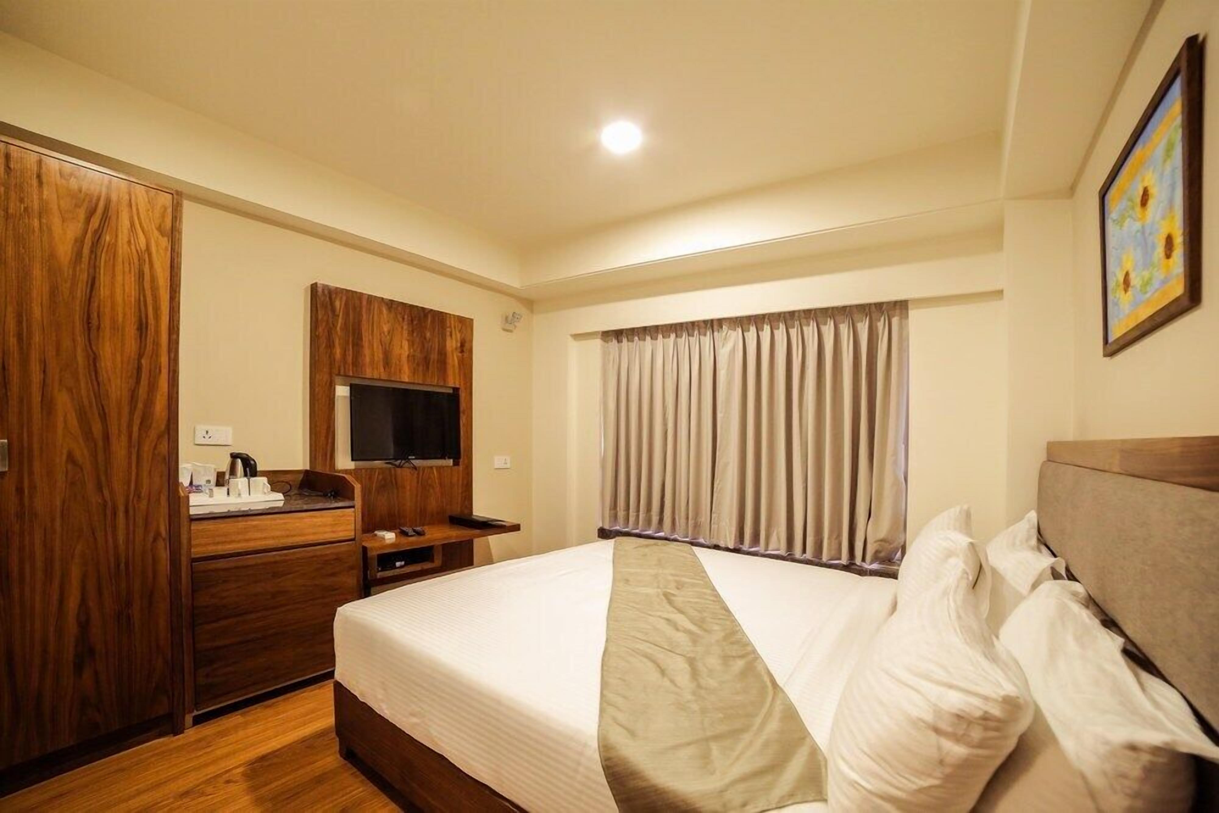Habitación de hotel con una cama grande, un armario de madera, un televisor de pantalla plana y una ventana con cortinas.
