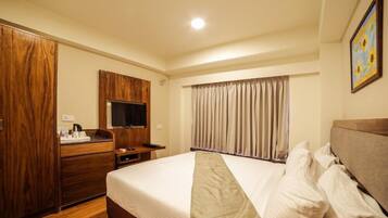 Habitación de hotel con una cama grande, un armario de madera, un televisor de pantalla plana y una ventana con cortinas.