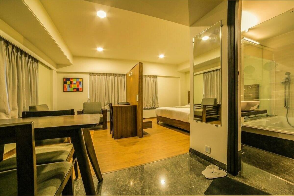 A hotel room with a bed, a desk, a chair, a small table, a mirror, and a bathroom with a shower and bathtub.