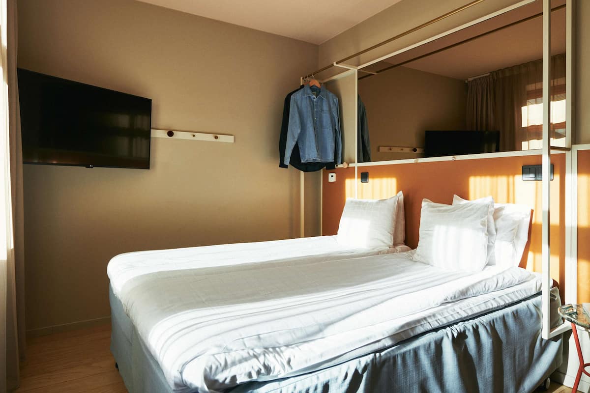A hotel room with a bed, a TV mounted on the wall, and a clothing rack.