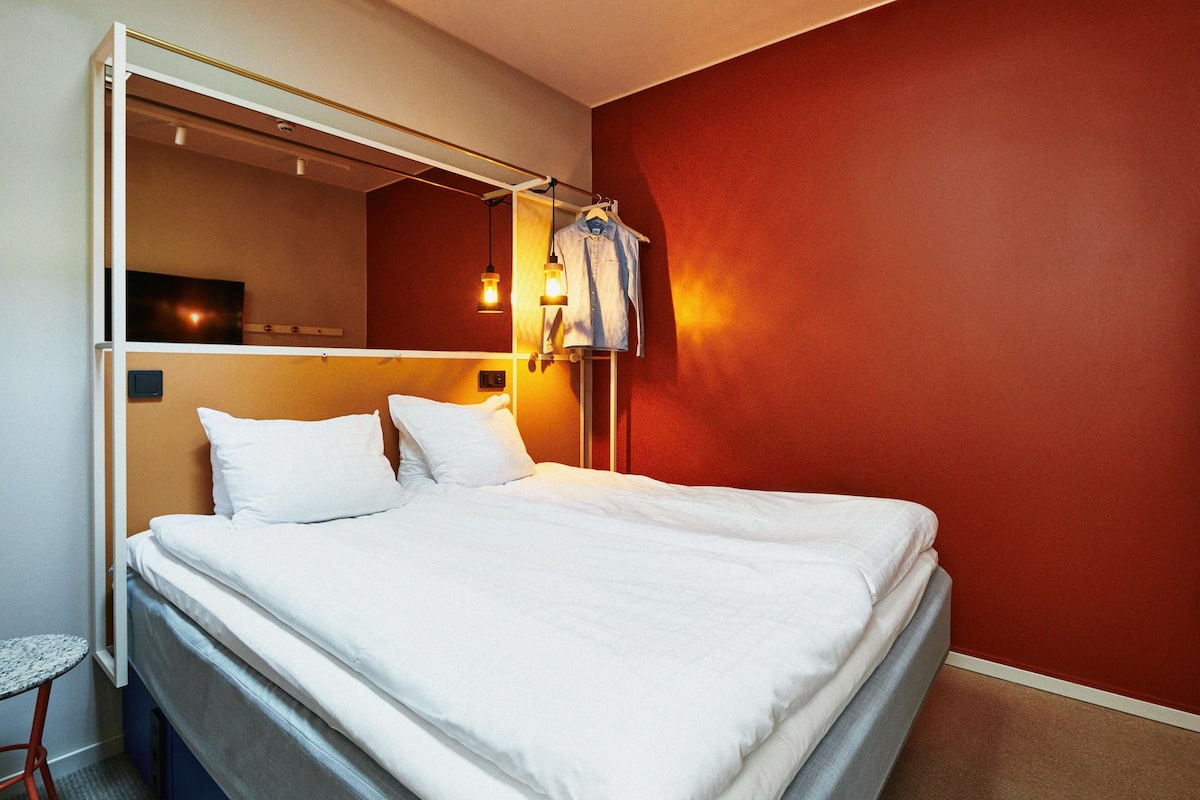 A hotel room with a bed, a small table, and a mirror.