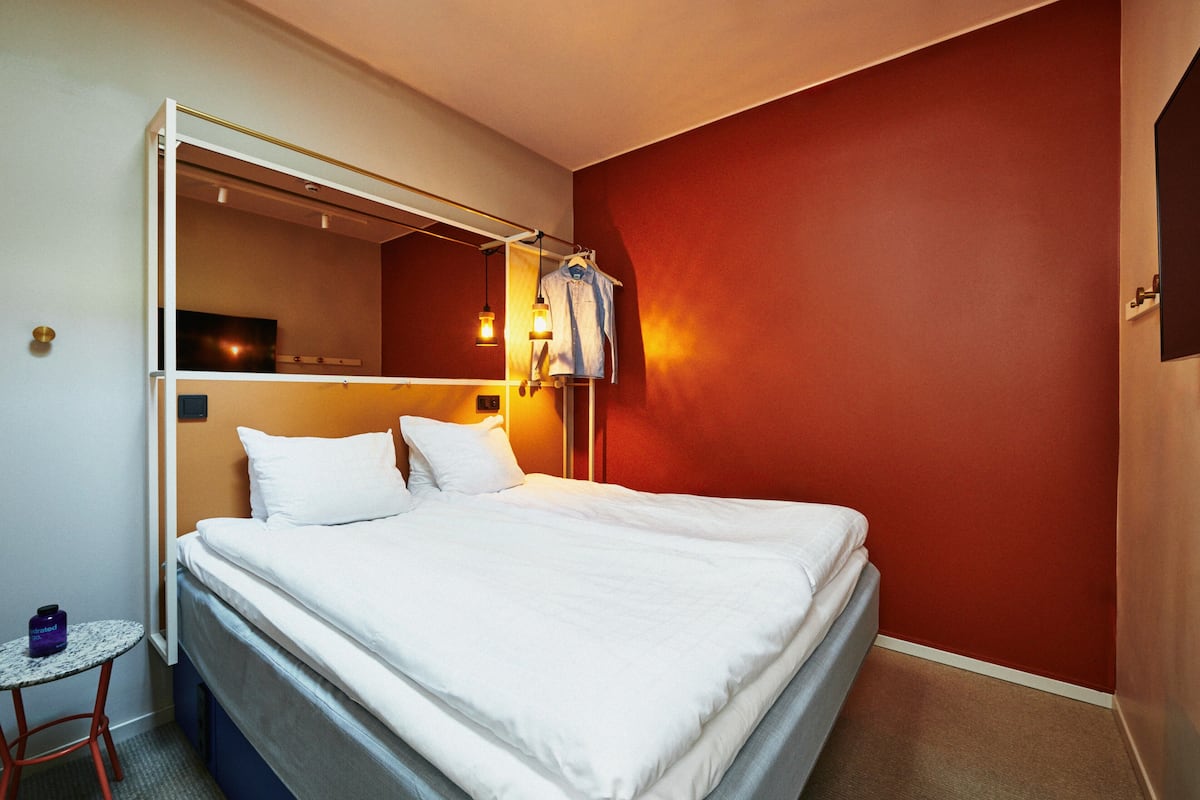 Una habitación de hotel con una cama, una mesita pequeña, una lámpara colgante y una pared de acento roja.
