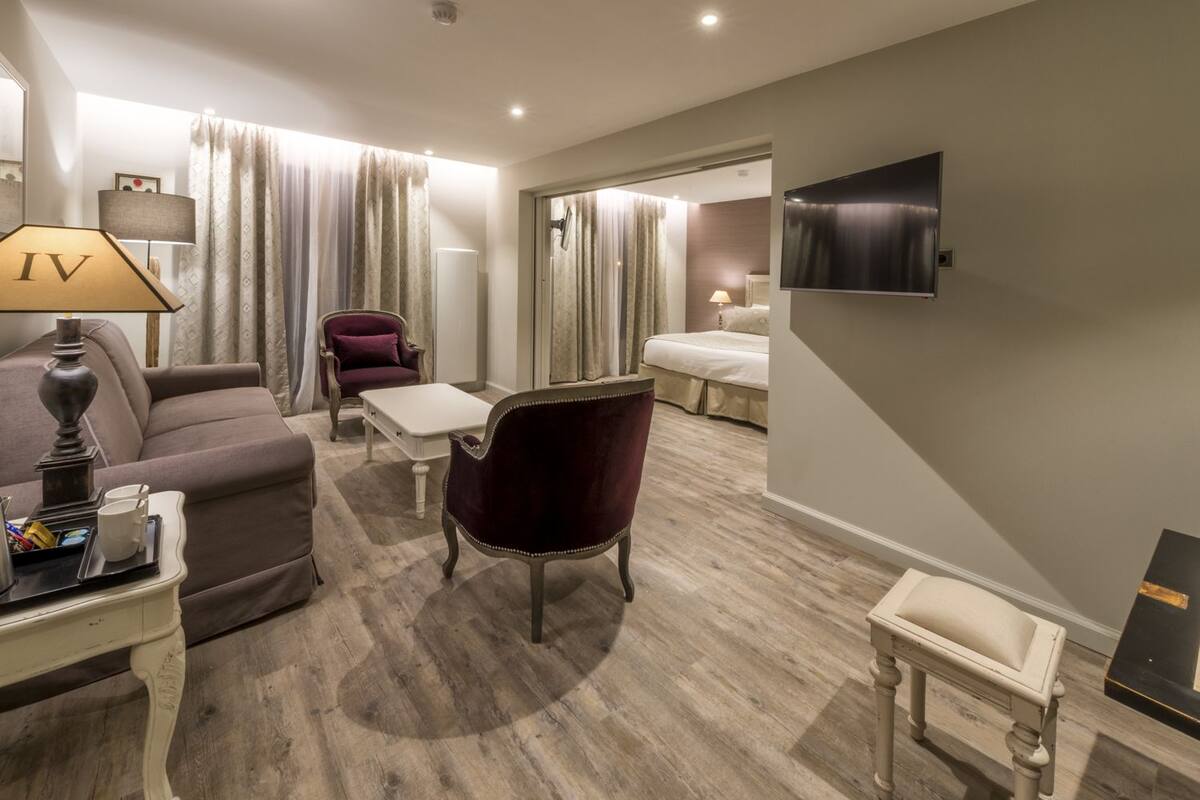 A hotel room with a sofa, armchair, small table, and a TV mounted on the wall.