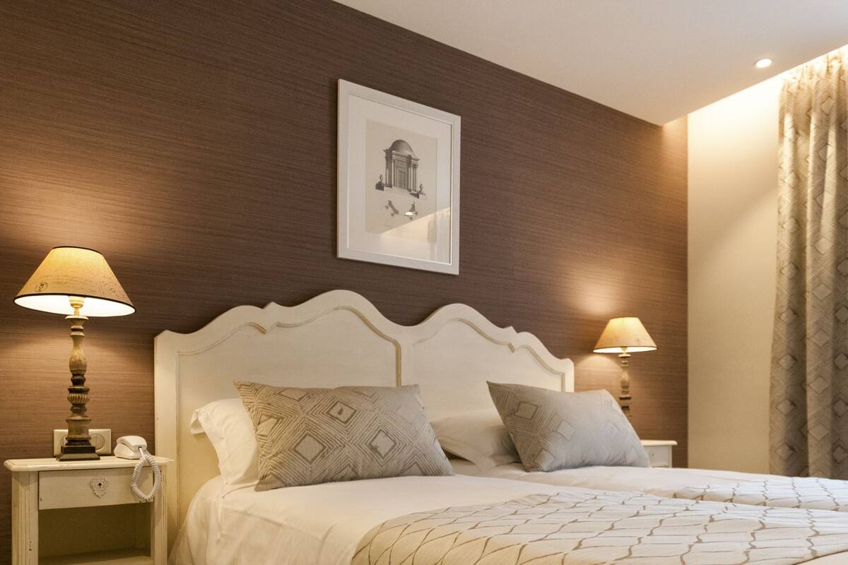 A hotel room with a white bed, two bedside lamps, a nightstand with a phone, and a framed picture on the wall.
