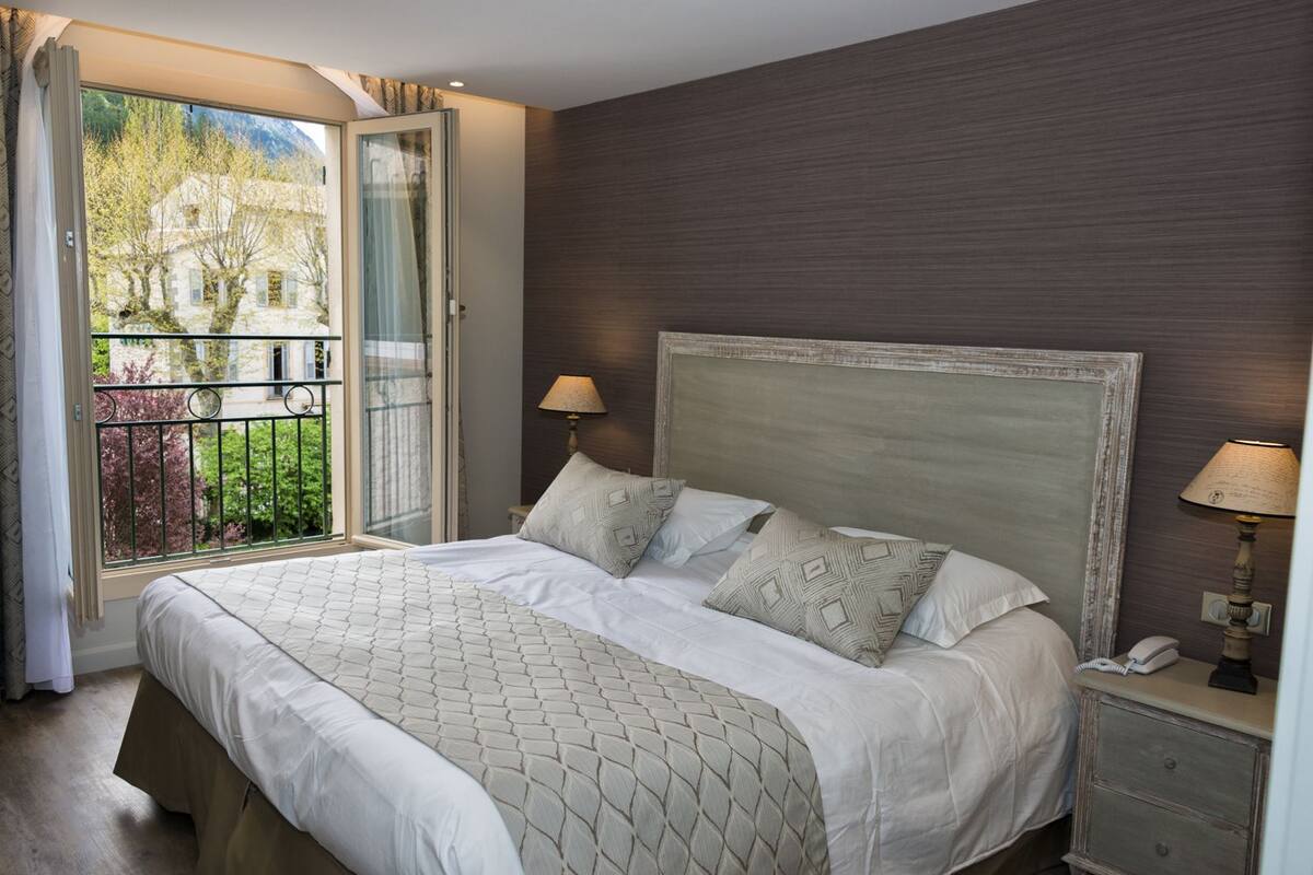 A bedroom with a large bed, a nightstand, a lamp, and a view of a building through a glass door.