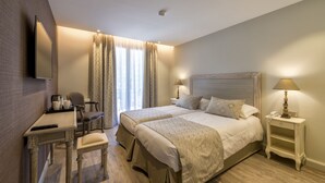 A hotel room with a bed, bedside tables, a desk with a chair, a TV, and a window with curtains. - Nouvel Hôtel du Commerce (Castellane)