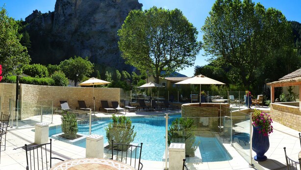 A pool area with lounge chairs and umbrellas, surrounded by stone walls and trees. - Nouvel Hôtel du Commerce (Castellane)