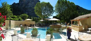 A pool area with lounge chairs and umbrellas, surrounded by stone walls and trees. - Nouvel Hôtel du Commerce (Castellane)