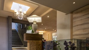 A lobby with a staircase, a chandelier, a large vase, and glass display cases with plants. - Nouvel Hôtel du Commerce (Castellane)