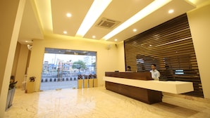 Zona de recepción de un hotel con suelo de mármol, mostrador de recepción y vistas a la calle.
