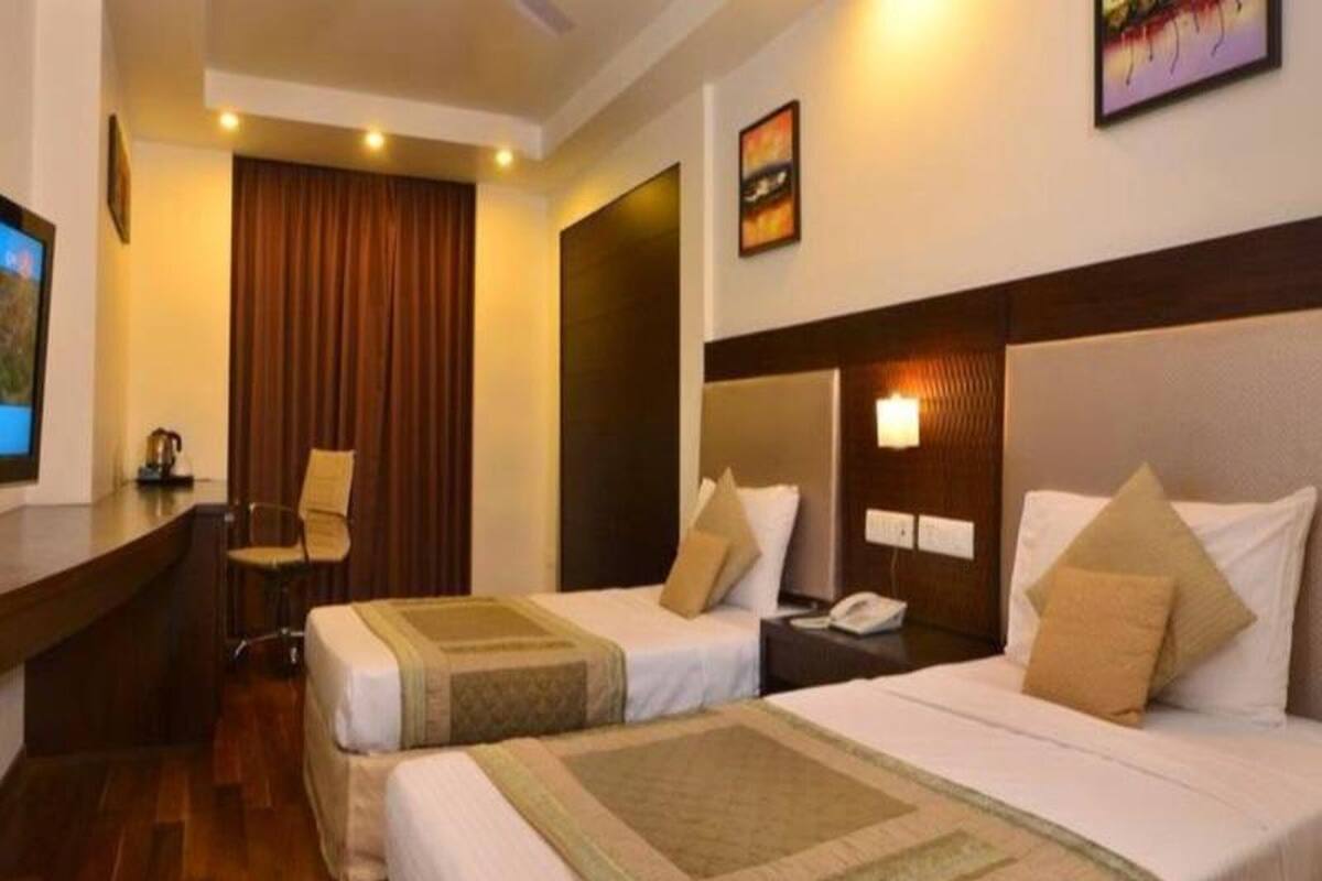 Habitación de hotel con dos camas, un escritorio, una silla y un televisor.