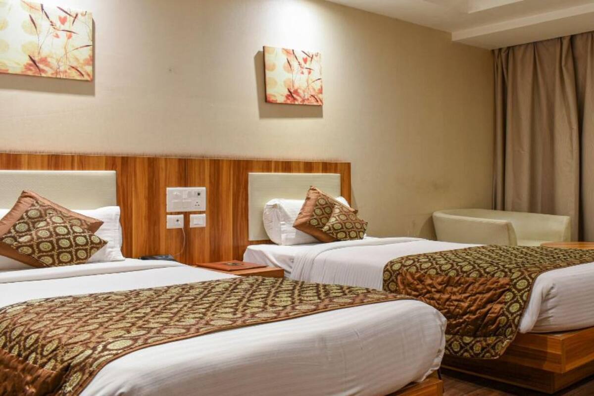 Habitación de hotel con dos camas, un cabecero de madera, un sillón blanco y obras de arte en las paredes.