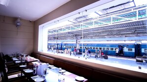 Un comedor con mesas preparadas para el servicio, y un ventanal con vistas a un andén de estación de tren.