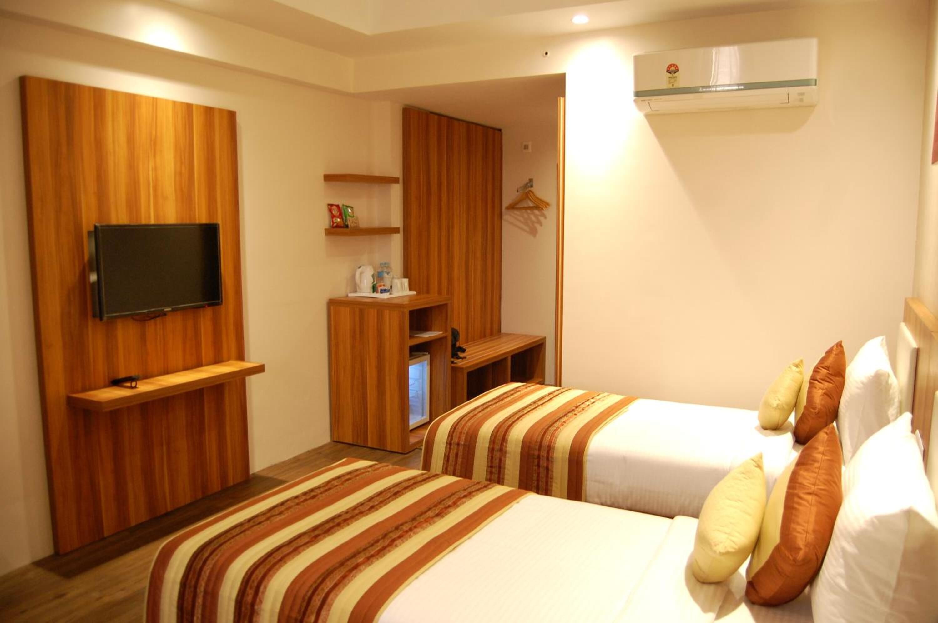 Habitación de hotel con dos camas, un televisor montado en un panel de madera, un escritorio con una silla y un equipo de aire acondicionado.