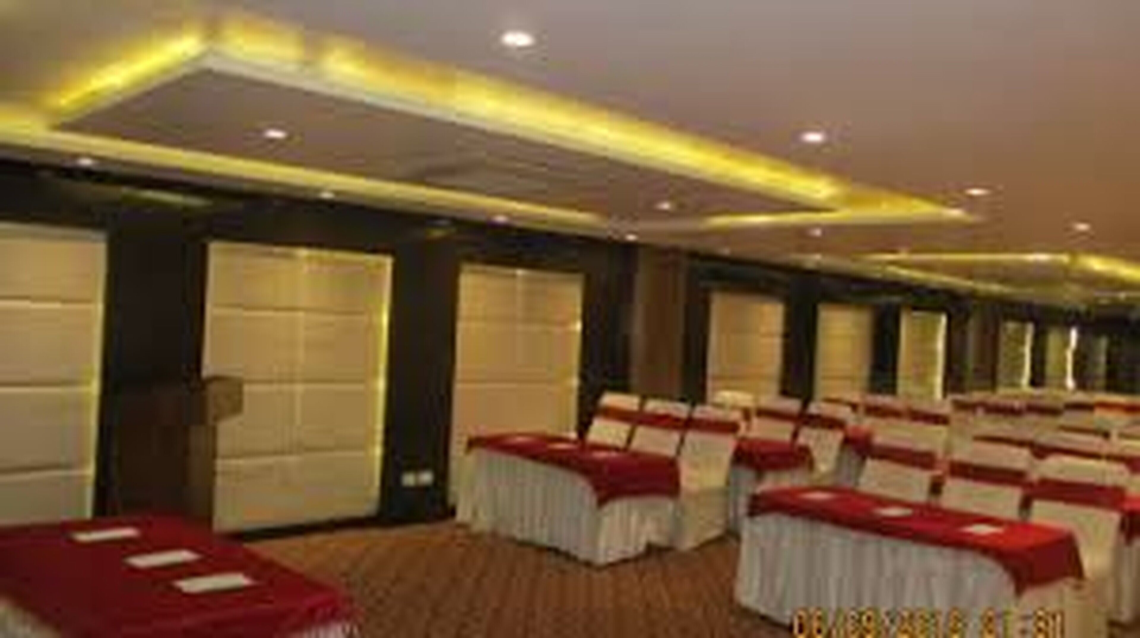 Un salón de conferencias con filas de mesas cubiertas con manteles blancos y rojos, sillas y ventanas amplias a lo largo de una pared.