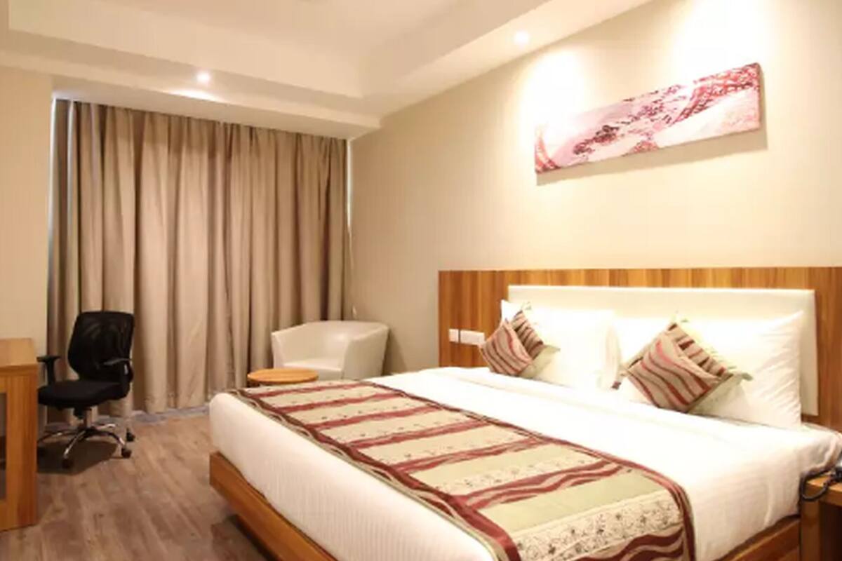 Una habitación de hotel con cama, escritorio, silla y un ventanal con cortinas.
