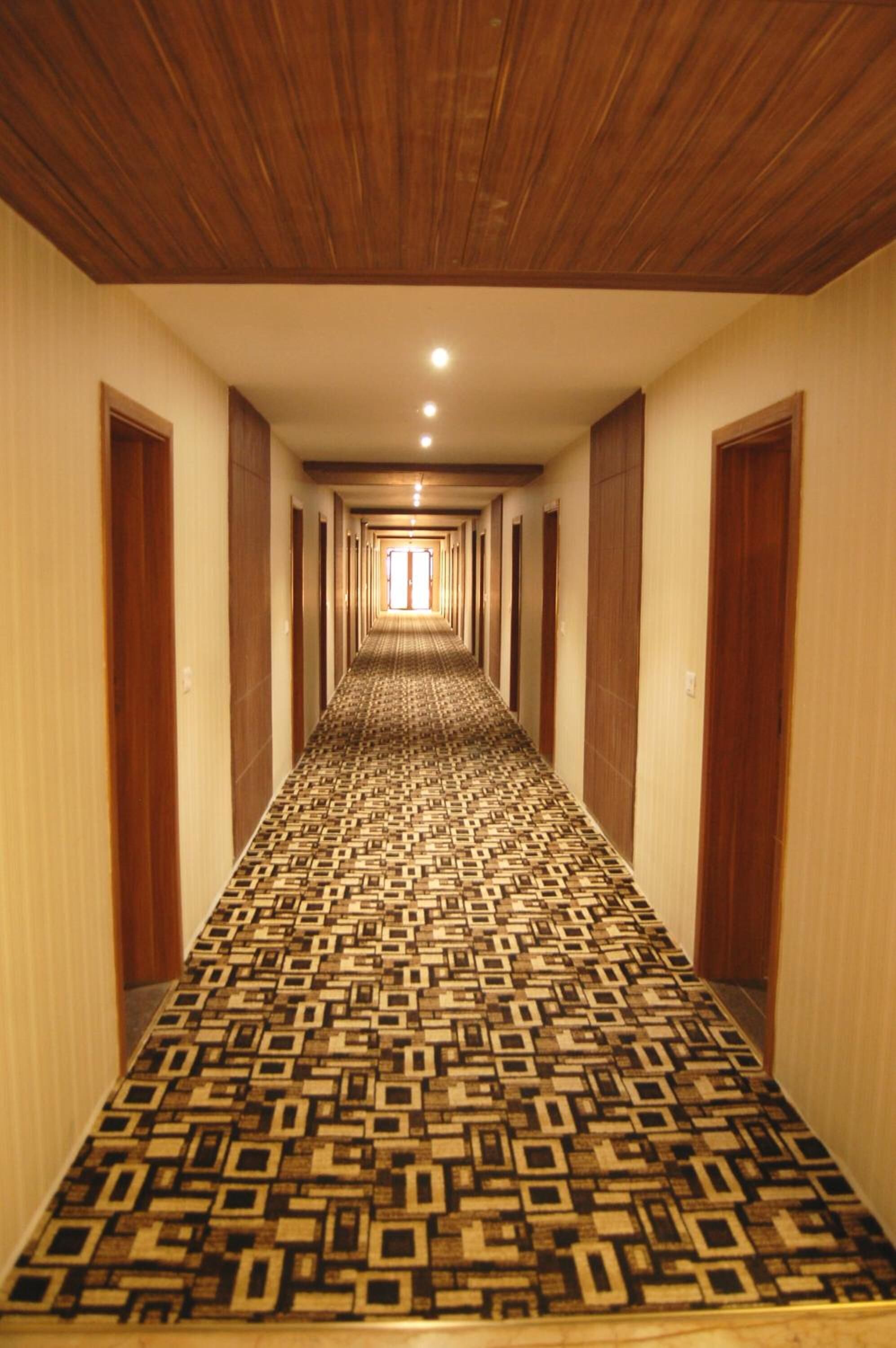 Un largo pasillo con alfombra estampada, puertas de madera y techo con paneles de madera.