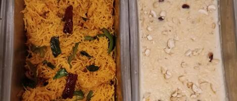 A stainless steel buffet with two dishes: one appears to be a yellow rice dish with green vegetables and red chilies, and the other is a creamy dish with nuts and raisins.
