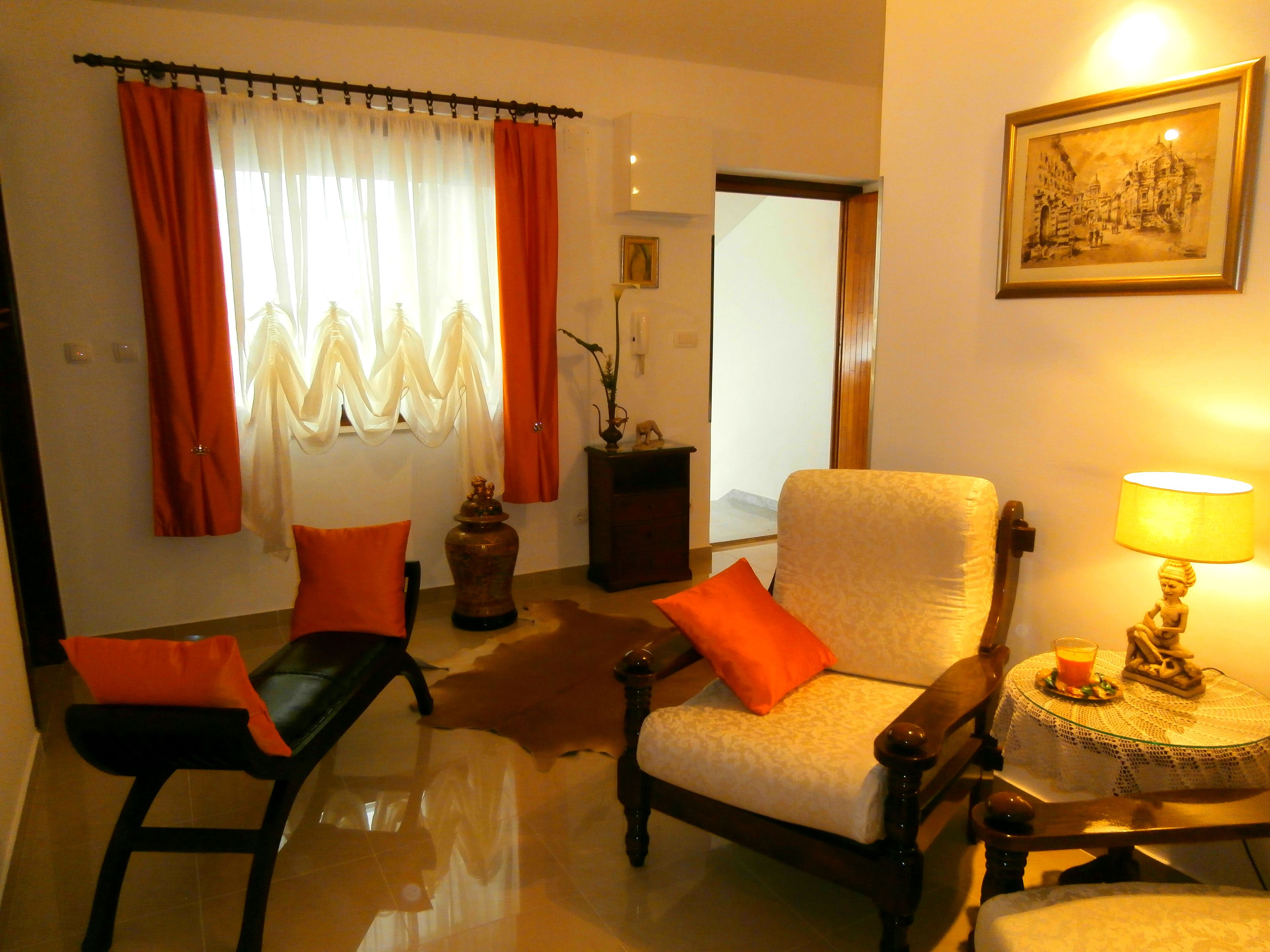 A living room with a sofa, a chair, a lamp, and a table with a vase and a picture on the wall.