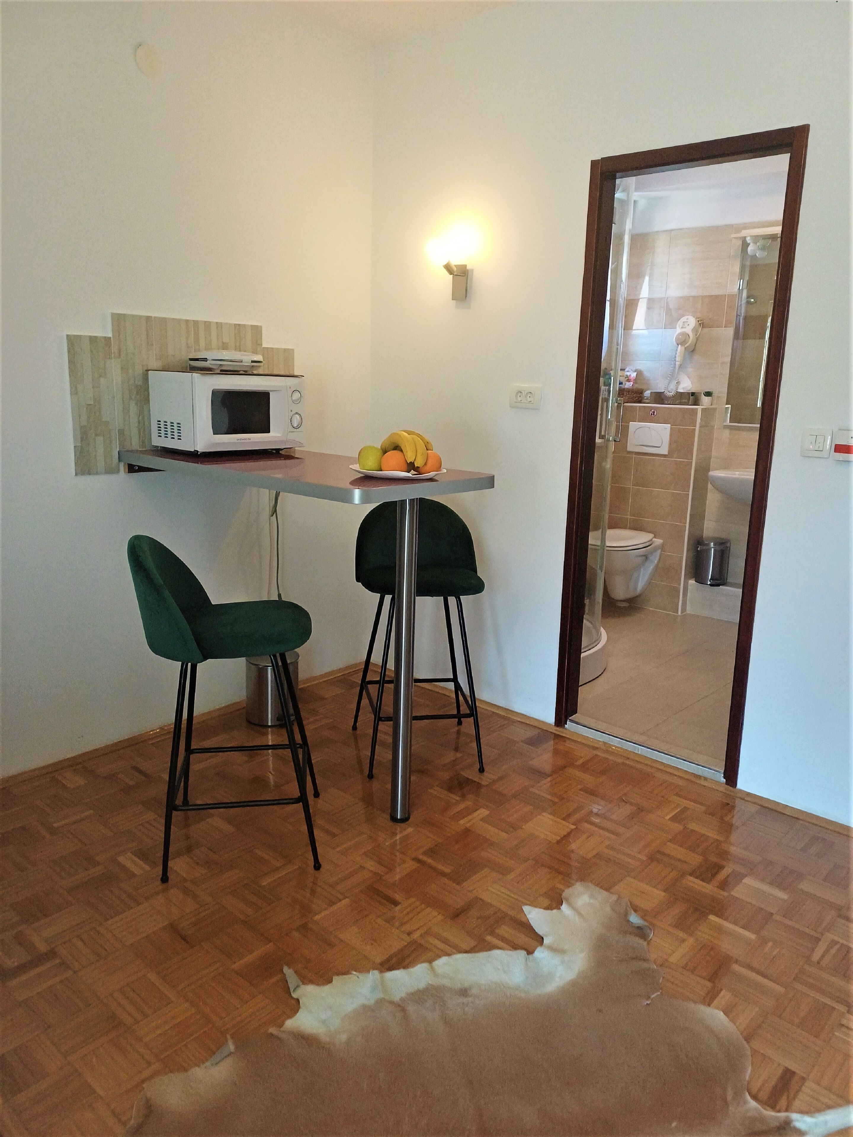 Una piccola zona pranzo con un forno a microonde, due sedie e una ciotola di frutta.