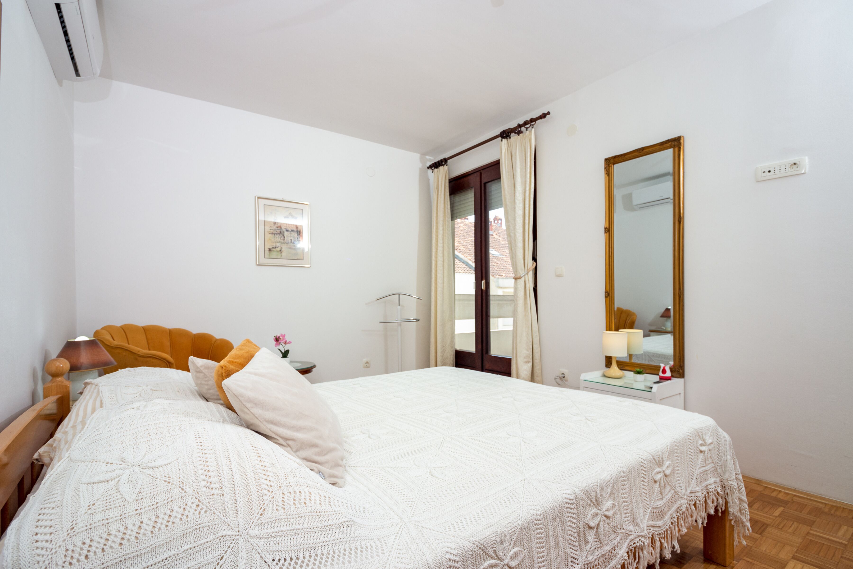 A bedroom with a bed, a bedside table with a lamp, a mirror, and a window with curtains.